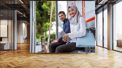 young Asian man and veiled woman smile at camera sitting together at bus stop Wall mural