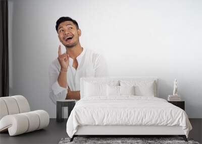 young asian man laughing with finger pointing for finding idea while standing on isolated background Wall mural