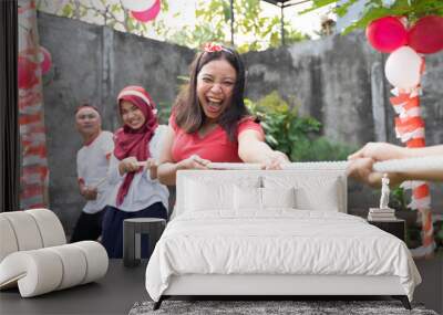 young asian woman in red scream out when tried to pull the rope hard during the tug-of-war competition at Indonesia's Independence Day celebrations Wall mural