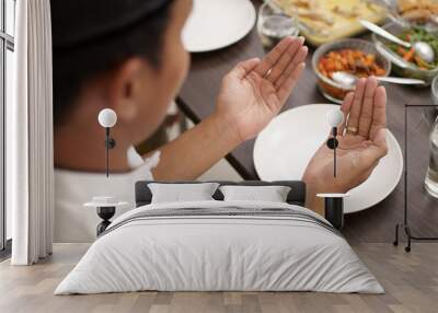 young man with muslim cap pray open his arm before having the meal Wall mural