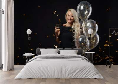 Brightfull expressions of happy emotions of  amazing blonde girl celebrating party on black background. Luxury black dresses, smiling, a glass of champagne, golden tinsels,  balloons, long curly hair Wall mural