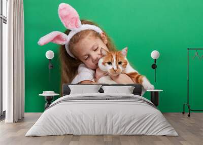 cute happy chikd girl with a real easter pet cat wearing ears on green background Wall mural