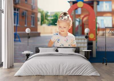 Cute little toddler girl excitedly plays on a multi-colored playground on a sunny day Wall mural