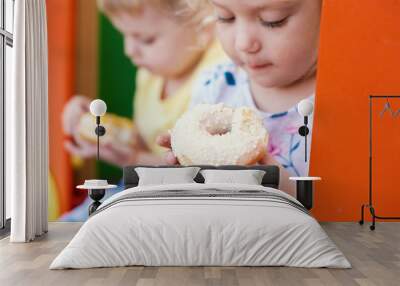 Cute toddler boy and girl  is eating donuts outdoor. children is having fun with cakes. Tasty food for kids. Funny time at playground with sweet food. Bright and stylish kids. Wall mural