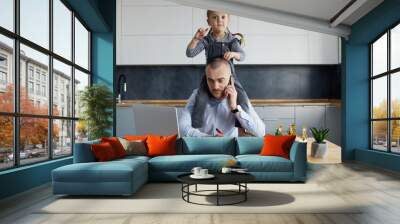 Father Working from home on laptop during quarantine. Little child girl make noise and distracts father from work on the kitchen office Wall mural