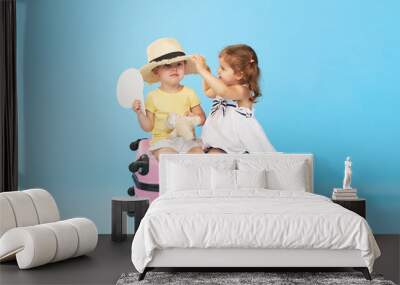 Happy kids sitting on colorful pink suitcase prepared for summer vacation. Young travelers. Little girl and boy, sister and brother, having fun isolated on blue background Wall mural