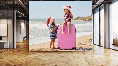 Happy little children girls in Santa hats with suitcase and globe. Kids having fun on summer vacation on Christmas and New year. Holiday Travel and adventure concept Wall mural