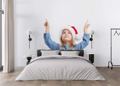 Happy smiling child girl in Santa hat and blue dress having fun on a red isolated background. points with hands up, empty area for text. Merry Christmas. Happy New Year Wall mural