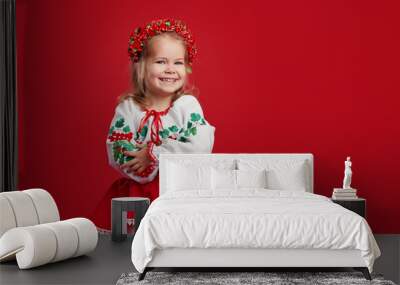 Happy smiling little girl in national Ukrainian folk costume, embroidered shirt, on red isolated background. On the head is a red wreath. The concept of national folklore of Russia and Ukraine Wall mural