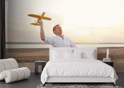 Happy young man playing with toy airplane on the beach on sunset. Dreams of being a child Wall mural