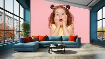 Portrait of a happy child. Cute little girl with a funny face on a pink background. Advertising baby products Wall mural