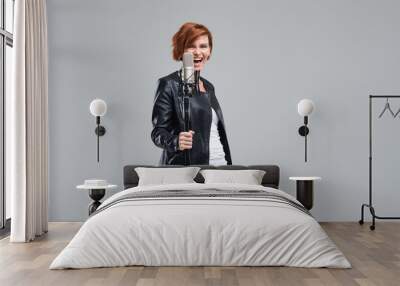 Portrait of rock singer wearing leather jacket and keeping static mic, sings a song loudly on grey background. Concept of rock music and rave Wall mural