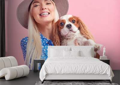 Portrait of smiling young blond woman in summer hat embracing king Charles spaniel dog. owner and pet relations concept. Veterinary health. Isolated front view on pink background. Wall mural