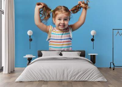 Portrait of surprised smiling cute little toddler girl. child standing isolated over blue background. Looking at camera and laughs Wall mural