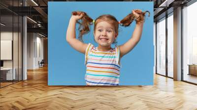 Portrait of surprised smiling cute little toddler girl. child standing isolated over blue background. Looking at camera and laughs Wall mural