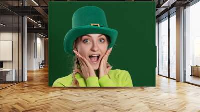 St. Patrick's Day leprechaun surprised model woman in green hat, funny clover shaped sunglasses, isolated on green background and smiling, having fun. Patrick Day party, wow face. Wall mural