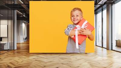 Studio shot of happy child boy celebrating holiday, unpacking gift box with excited face, posing over yellow background Wall mural