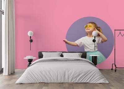 Surprised Little Child girl in heart shap sunglasses looking out of a pink round hole. Banner. Happy girl Looking at camera. Wow funny face Wall mural