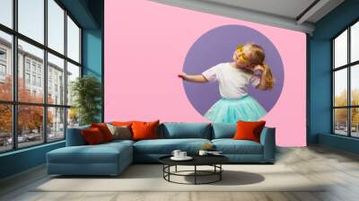 Surprised Little Child girl in heart shap sunglasses looking out of a pink round hole. Banner. Happy girl Looking at camera. Wow funny face Wall mural