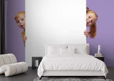 Two little children holding a white banner on purple background. Funny Faces Wall mural