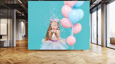 Unicorn girl. Joyful child girl in elegant tulle dress and unicorn headband celebrates birthday  party and blowing multicolored confetti on cyan background Wall mural