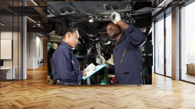 African mechanic workers fixing underneath car and talking about work in garage Wall mural