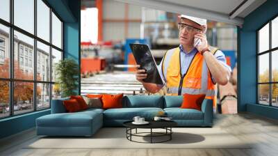 male factory workers or engineer talking on smartphone and looking information on clipboard in factory Wall mural