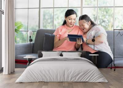 mother using tablet computer with a girl down syndrome or her daughter, smiling and enjoying on sofa Wall mural