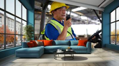 senior worker using walkie talkie and holding steering wheel on forklift truck in the factory Wall mural