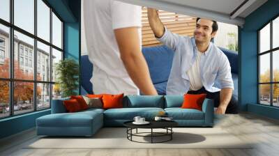 young handsome man giving hi five pose with his friends in a living room Wall mural