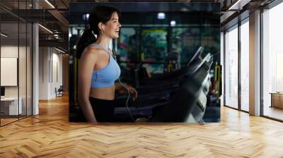 young sports woman working out with wired earbuds and running on treadmill in gym Wall mural