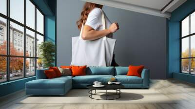 A woman is carrying a canvas tote bag. The tote bag mockup is white with grey background Wall mural