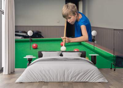 Cute boy in blue t shirt plays billiard or pool in club. Young Kid learns to play snooker. Boy with billiard cue strikes the ball on table. Active Leisure, sport, hobby concept Wall mural