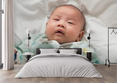 Close-up of male newborn baby wearing hat on his head with relaxed and happy smiling face lying on white bed. Wall mural