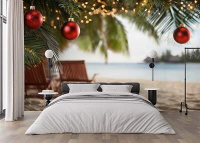 Red christmas ornaments and string lights adorn a palm tree on a tropical beach, with two unoccupied lounge chairs nearby Wall mural