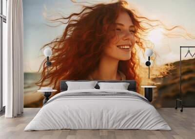 Young happy woman with curly red hair on a golden hour windy beach, close up portrait. Wall mural