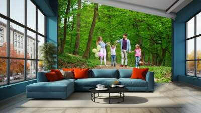 Family father and mother with two kids walking in summer green city park on picnic, happy holidays parents and children on nature Wall mural