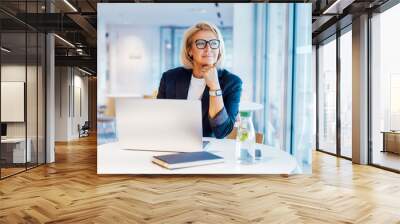 50's confident mature businesswoman dreamy looking at window, middle-aged experienced senior female professional working on laptop in open space office. Female entrepreneur working remotely. Wall mural