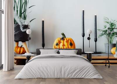 Halloween pumpkin Jack-o-lantern with spiders on it, black candles and decorated home plants standing on modern wooden cabinet. Seasonal living room interior. holidays, decoration and party concept Wall mural