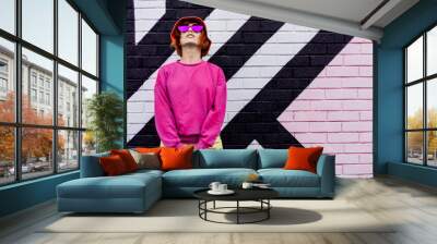 Hipster fashion young woman in trendy magenta color sweatshirt and sunglasses and bucket hat posing on the painted brick wall background. Color of the 2023 year. Urban city street fashion. Wall mural