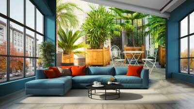 Metal garden furniture, stools and table standing in tropical plants orangery with palms in wooden flowerbeds. Relaxing time in biophilic interior style. Greenhouse cafe concept. Copy space Wall mural