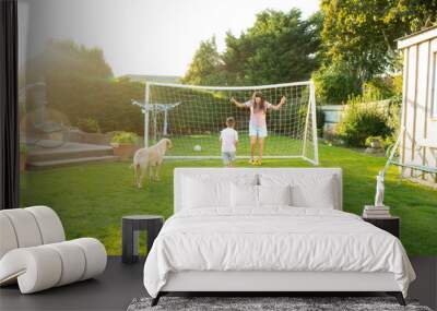 Young mother and son plays soccer with dog and have fun together. Happy family playing football with pet. Fun Playing Games in Backyard Lawn on Sunny Summer Day. Motherhood, childhood, togetherness Wall mural