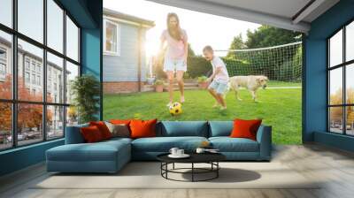 Young mother and son plays soccer with dog and have fun together. Happy family playing football with pet. Fun Playing Games in Backyard Lawn on Sunny Summer Day. Motherhood, childhood, togetherness Wall mural