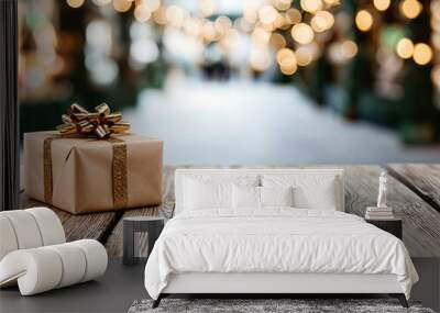 Wrapped christmas gift with golden ribbon lying on a wooden table background with festive lights bokeh Wall mural