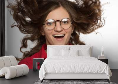 Beautiful curly brunette girl in a shirt and glasses laughs and flings her hair up over a white background Wall mural