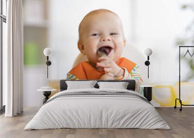 Cheerful baby child eats food itself with spoon. Portrait of happy kid boy in high-chair. Wall mural