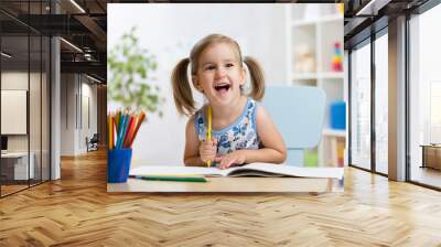 Expressive kid girl draws sitting at table in room in nursery Wall mural