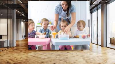 Group of nursery babies toddlers eating healthy food lunch break together with kindergartener Wall mural