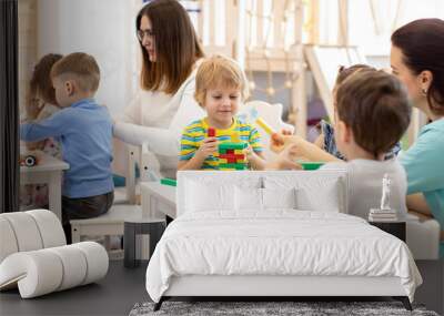 Group of preschool children and teacher playing with building blocks together in kindergarten Wall mural