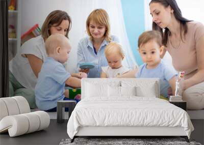 Group of toddlers and their mothers playing with colorful educational toys in nursery room Wall mural